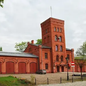 Zabytkowa remiza strażacka z wieżą na ł&oacute;dzkim Księżym Młynie w pochmurny dzień.